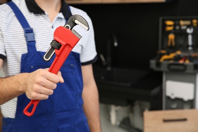 Photo of Male plumber holding pipe wrench in kitchen, closeup with space for text. Repair service