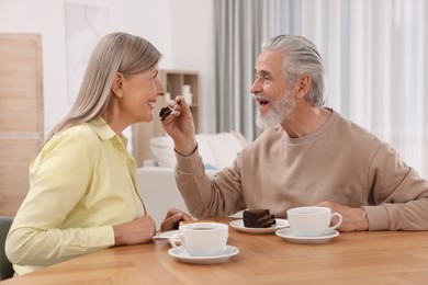 Photo of Affectionate senior couple having breakfast at wooden table in room