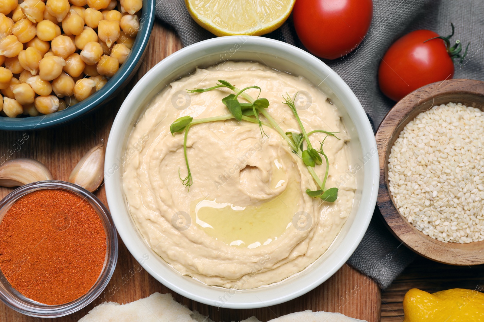 Photo of Delicious hummus with microgreens and different ingredients on wooden table, flat lay