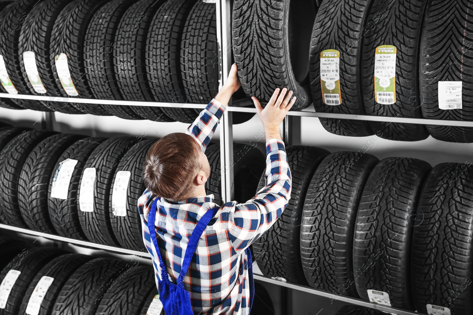 Photo of Young male mechanic with car tires in automobile service center