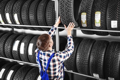 Young male mechanic with car tires in automobile service center