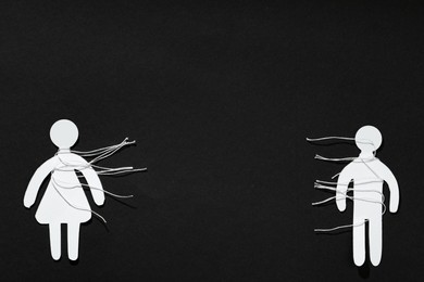 Photo of Divorce concept. Paper human figures with cut white threads on black background, flat lay. Space for text