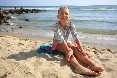 Photo of Happy little girl on sandy beach near sea