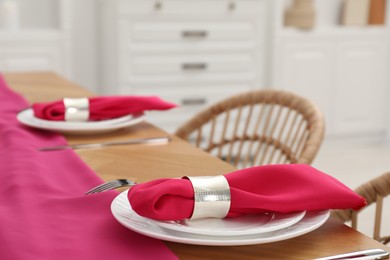 Table setting. Plates with pink napkins, decorative rings and cutlery in dining room