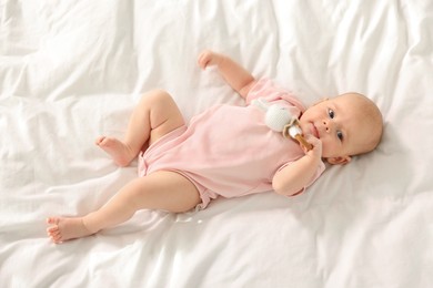 Photo of Cute little baby with toy on white sheets, top view
