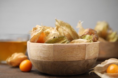 Ripe physalis fruits with calyxes in bowl on wooden table, closeup