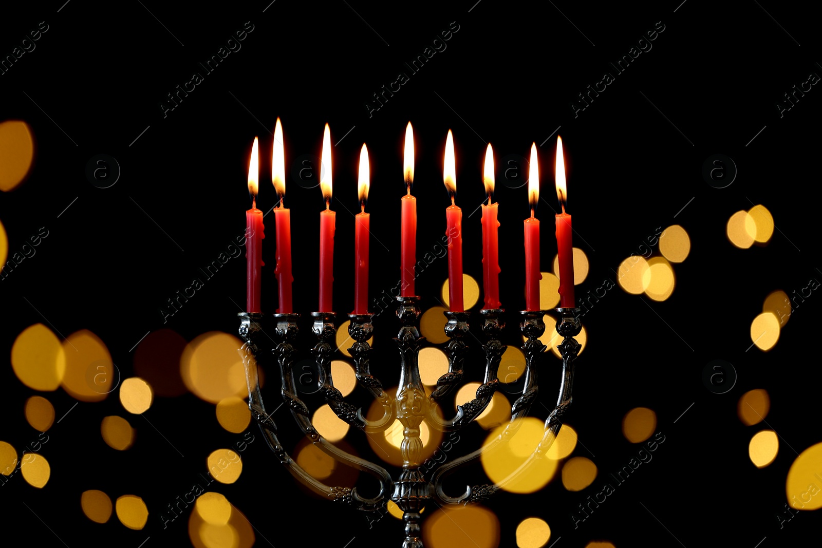 Photo of Silver menorah with burning candles against dark background and blurred festive lights. Hanukkah celebration