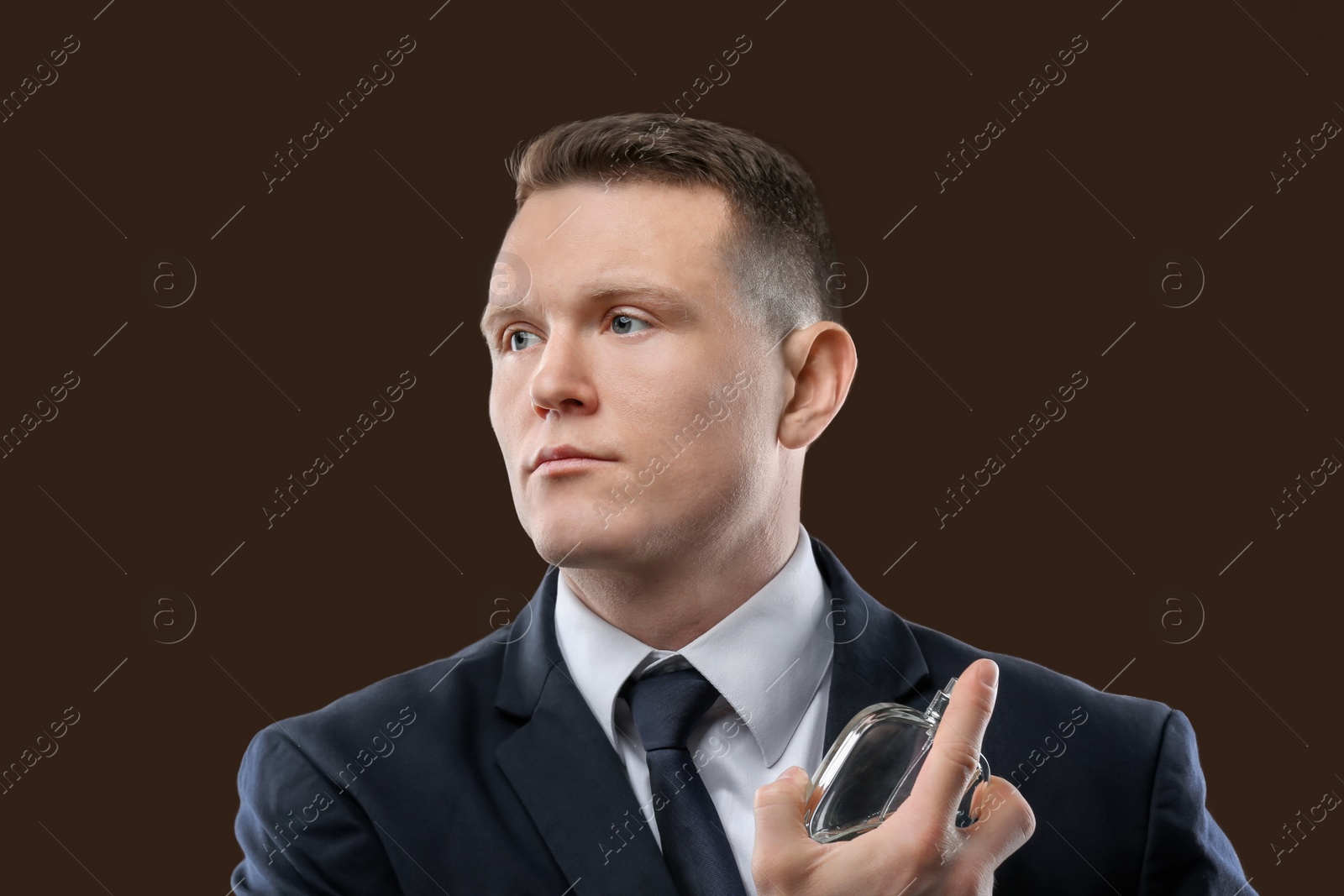 Photo of Handsome man in suit using perfume on dark background