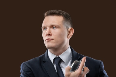 Handsome man in suit using perfume on dark background