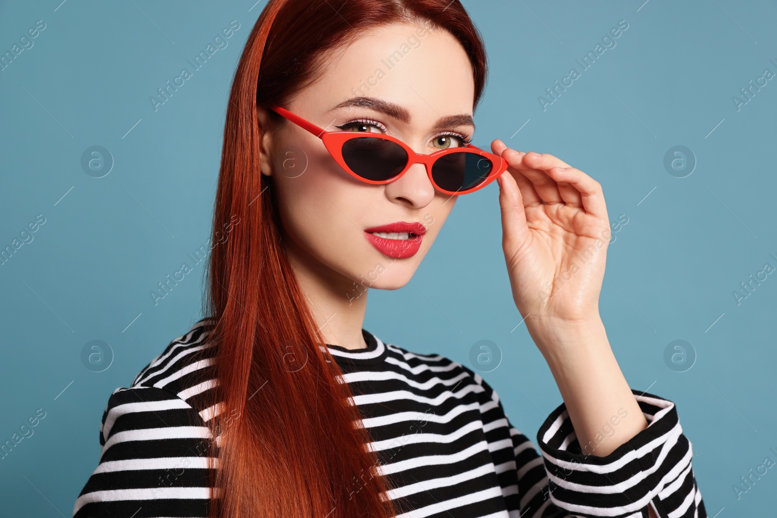 Photo of Stylish woman with red dyed hair and sunglasses on light blue background