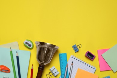 Photo of Different stationery and school bell on yellow background, flat lay. Space for text