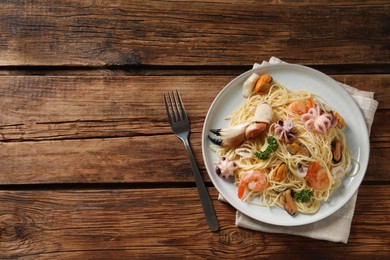 Delicious spaghetti with seafood served on wooden table, flat lay. Space for text