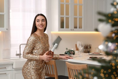 Photo of Christmas mood. Smiling woman holding bottle of wine at table in kitchen