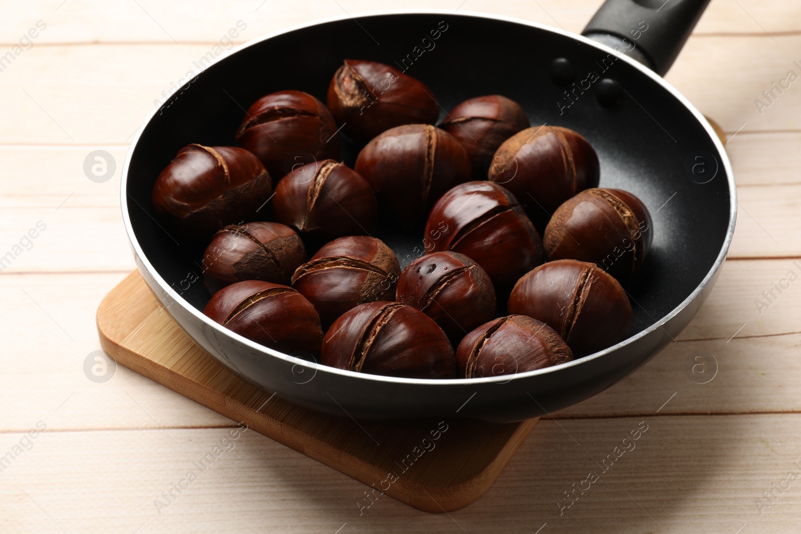 Photo of Roasted edible sweet chestnuts in frying pan on wooden table