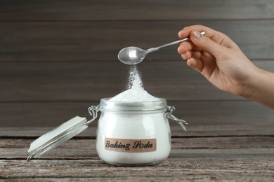 Woman pouring baking soda from spoon into jar at wooden table, closeup