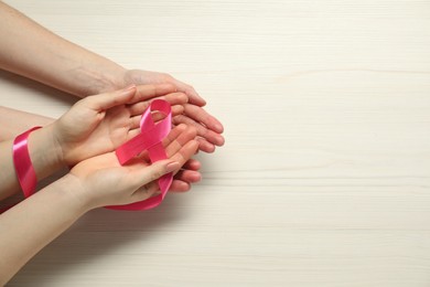 Breast cancer awareness. Women holding pink ribbon at white wooden table, top view. Space for text