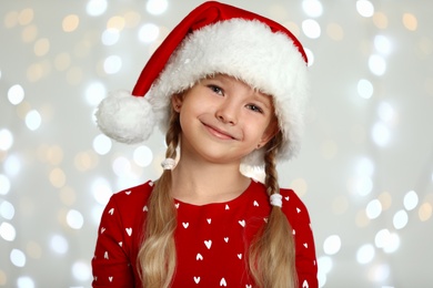 Photo of Happy little child in Santa hat against blurred festive lights. Christmas celebration