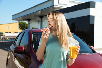 Photo of Beautiful young woman with juice eating doughnut near car at gas station