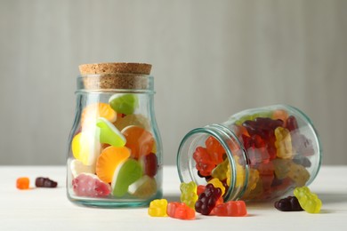 Delicious gummy candies in glass jars on white wooden table