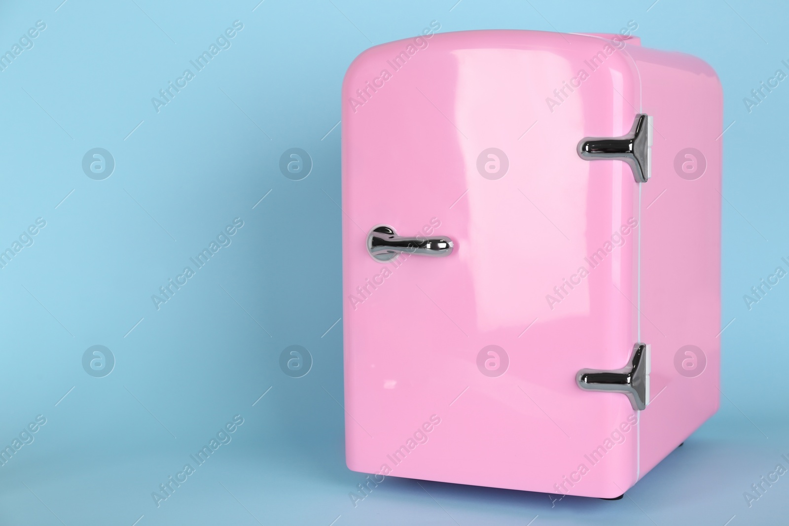 Photo of Pink cosmetics refrigerator on light blue background, space for text