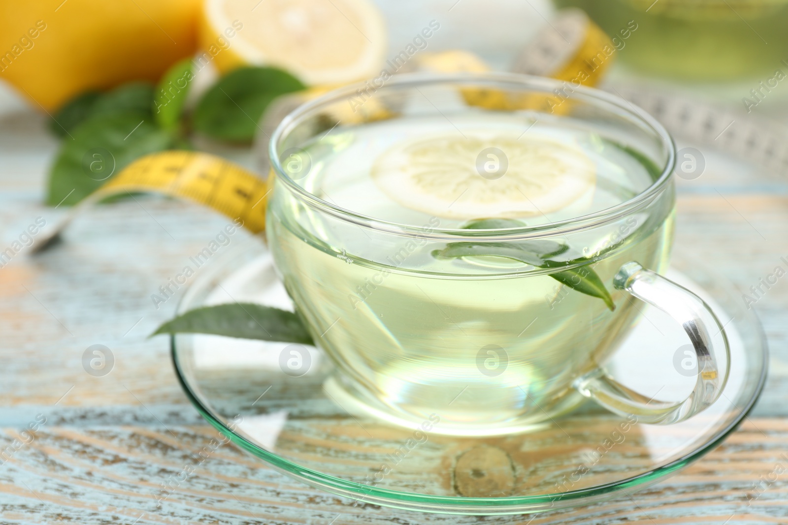 Photo of Glass cup of diet herbal tea with green leaves and lemon on wooden table, closeup