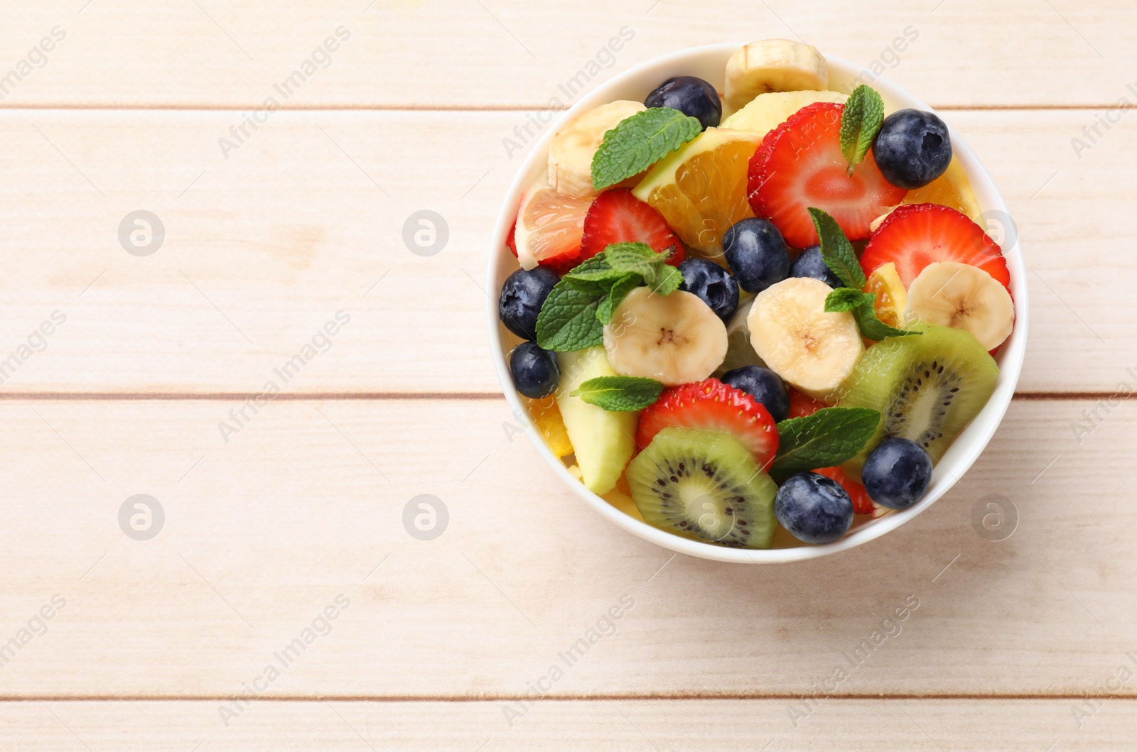 Photo of Tasty fruit salad in bowl on wooden table, top view. Space for text