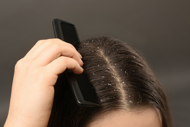 Image of Woman with comb and dandruff in her dark hair on grey background, closeup