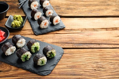 Photo of Tasty sushi rolls served on wooden table. Space for text