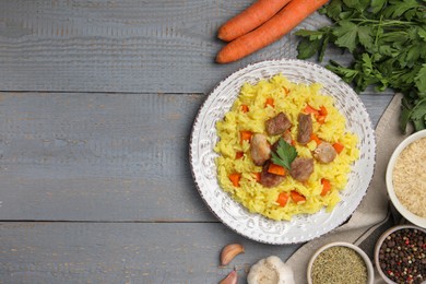 Delicious pilaf with meat and ingredients on grey wooden table, flat lay. Space for text