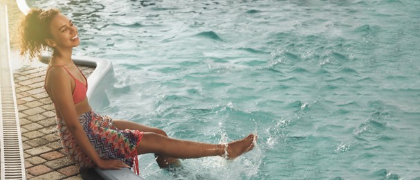 Beautiful African American woman resting near outdoor swimming pool on sunny day, banner design