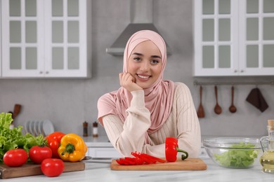 Portrait of Muslim woman near vegetables at white table in kitchen