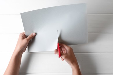 Photo of Woman cutting paper with scissors at white wooden background, top view