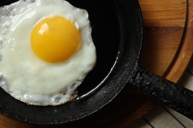 Photo of Frying pan with tasty cooked egg on wooden board, top view