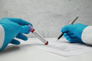 Photo of Liver Function Test. Laboratory worker holding tube with blood sample while working at white table, closeup
