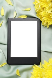 Photo of E-book reader with flowers on silk fabric, flat lay. Space for text