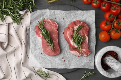 Photo of Fresh raw meat with rosemary, tomatoes and spices on grey wooden table, flat lay