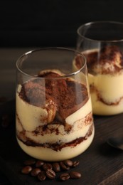 Photo of Delicious tiramisu in glasses and coffee beans on wooden board, closeup
