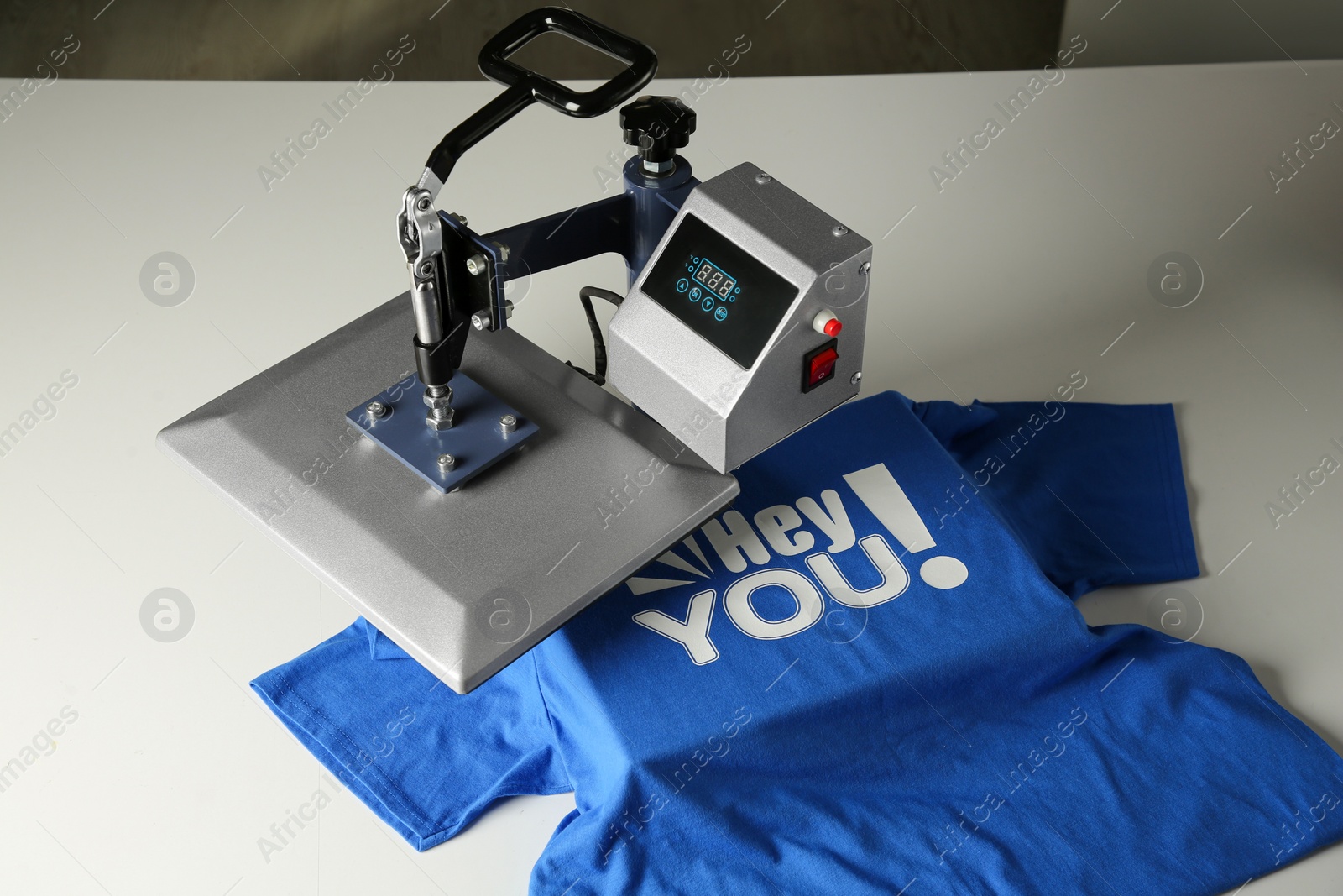 Photo of Printing logo. Heat press with blue t-shirt on white table