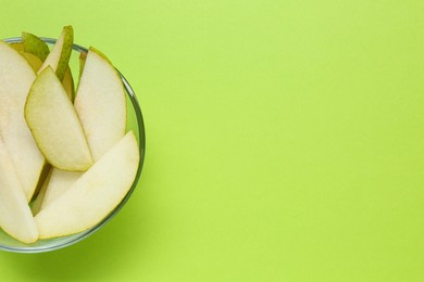 Photo of Sliced fresh pear in bowl and space for text on green background, top view. Finger food