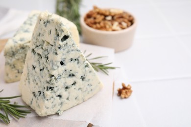 Photo of Tasty blue cheese with rosemary and walnuts on white tiled table, closeup. Space for text