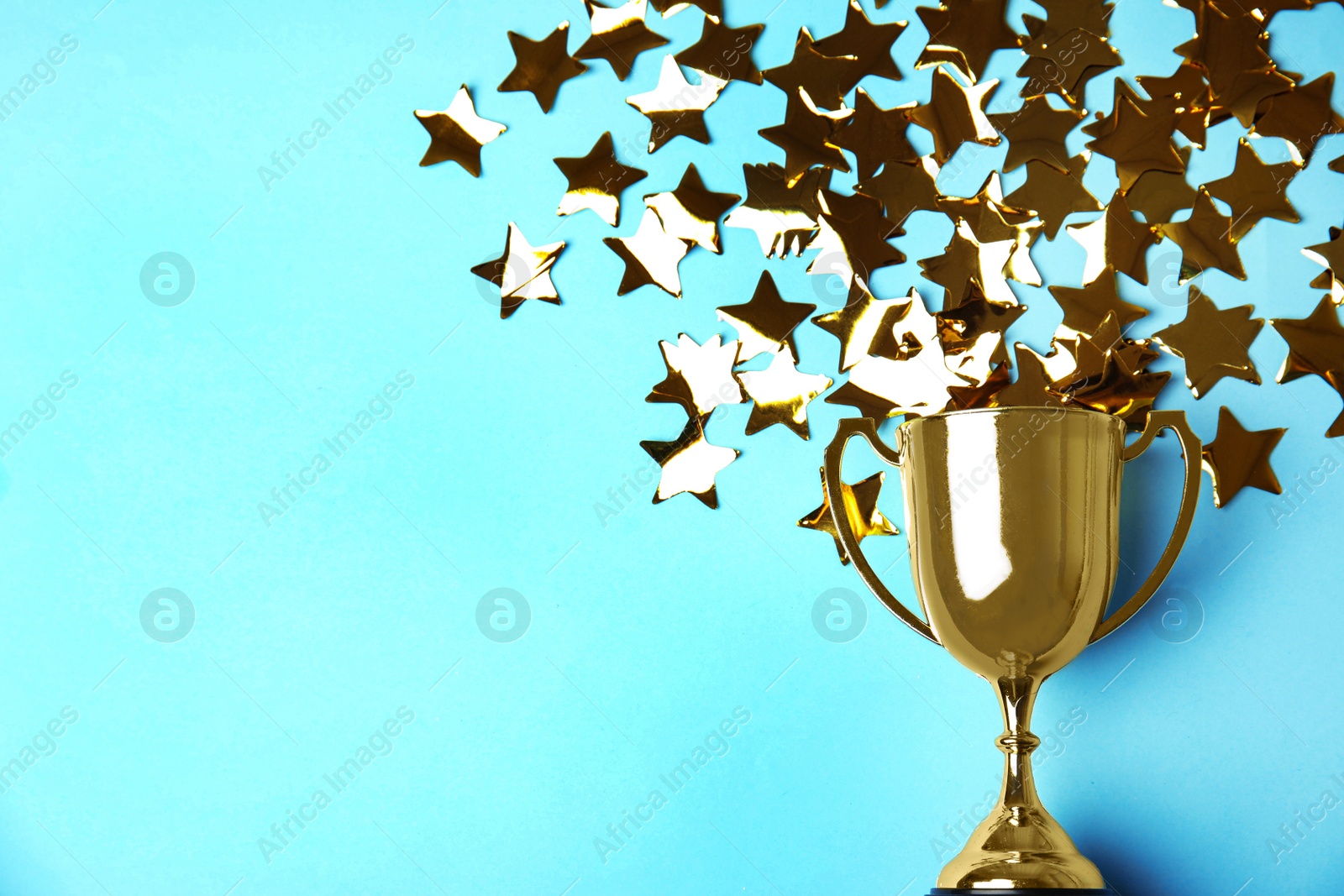 Photo of Gold trophy cup and confetti on light blue background, flat lay. Space for text