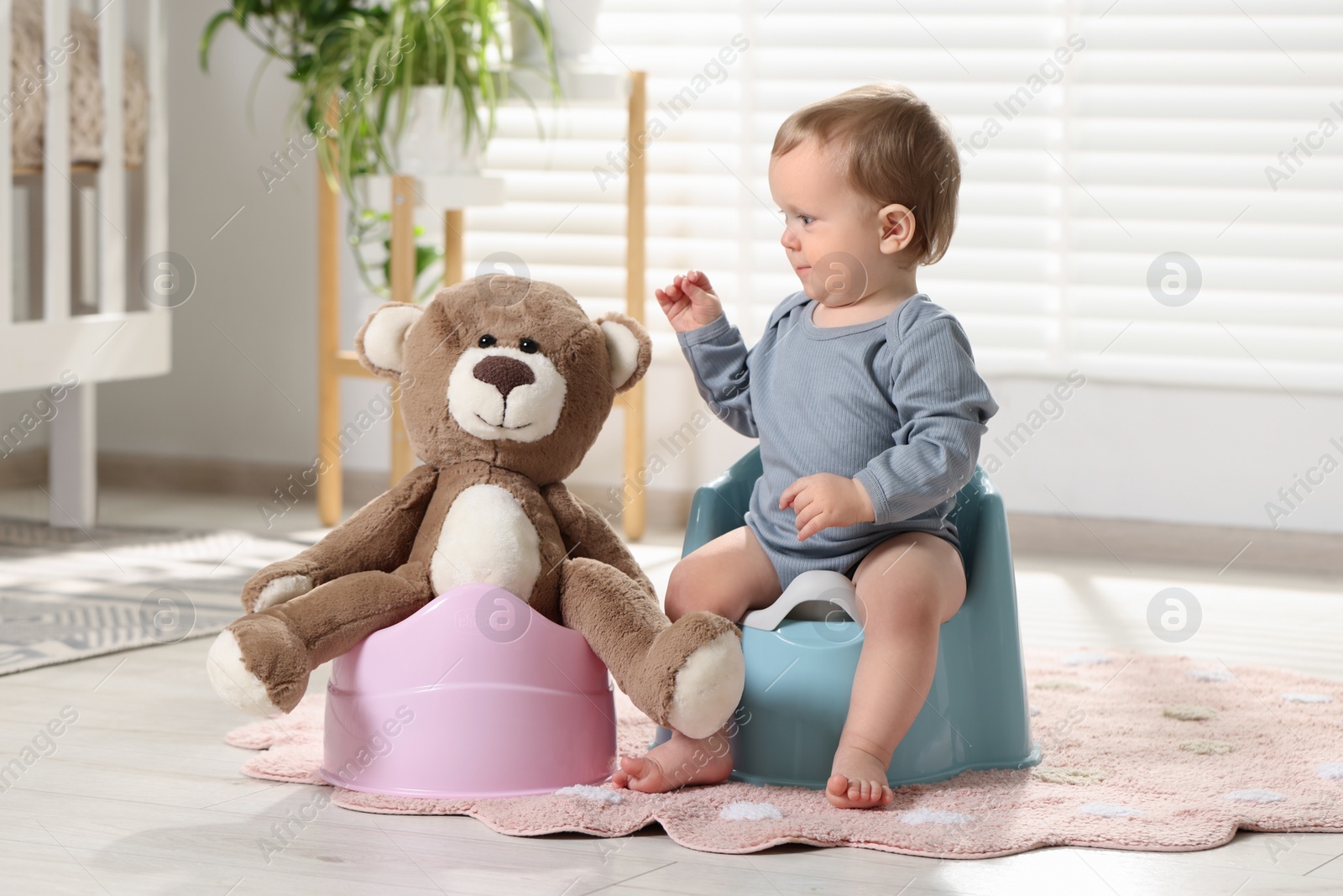 Photo of Little child and teddy bear sitting on plastic baby potties indoors