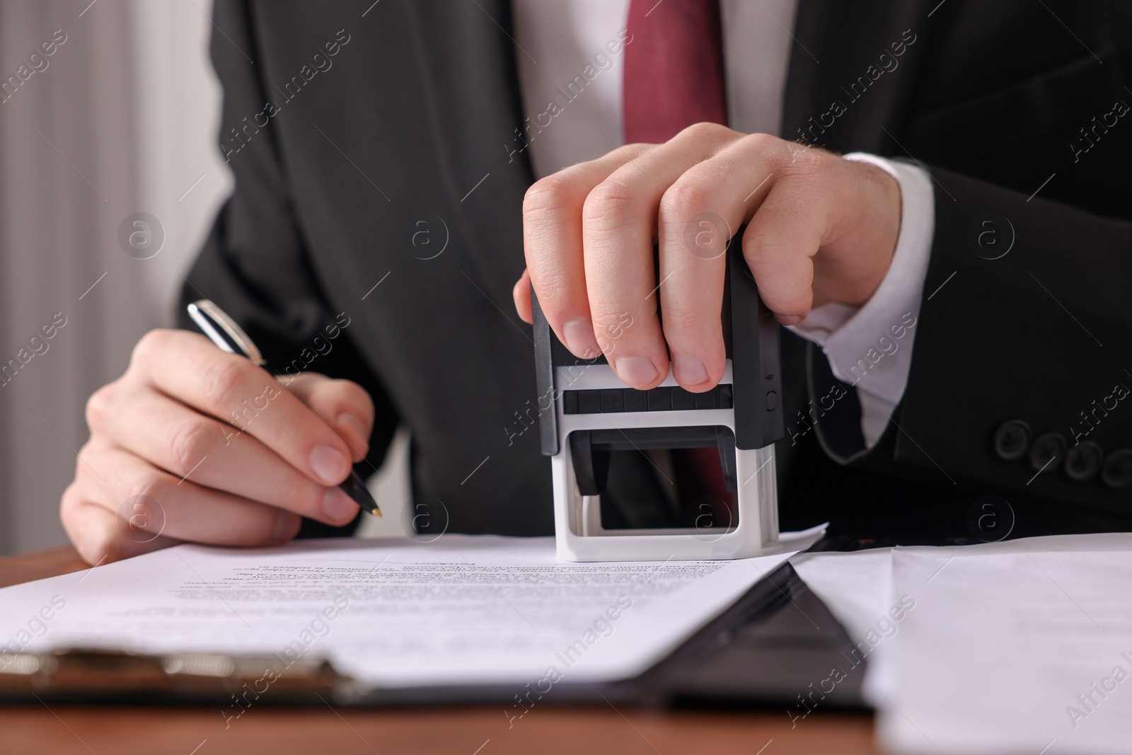 Photo of Notary with pen stamping document at table in office, closeup