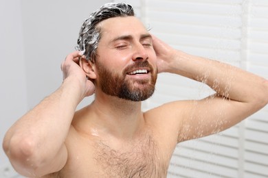 Photo of Happy man washing his hair with shampoo in shower