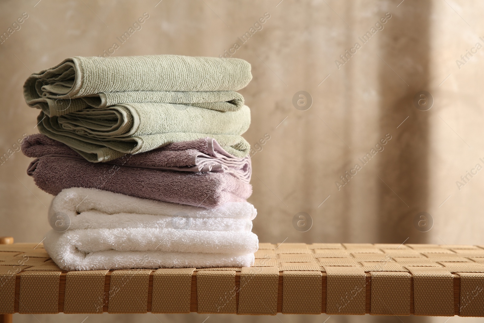 Photo of Stack of soft towels on wicker bench indoors, closeup. Space for text