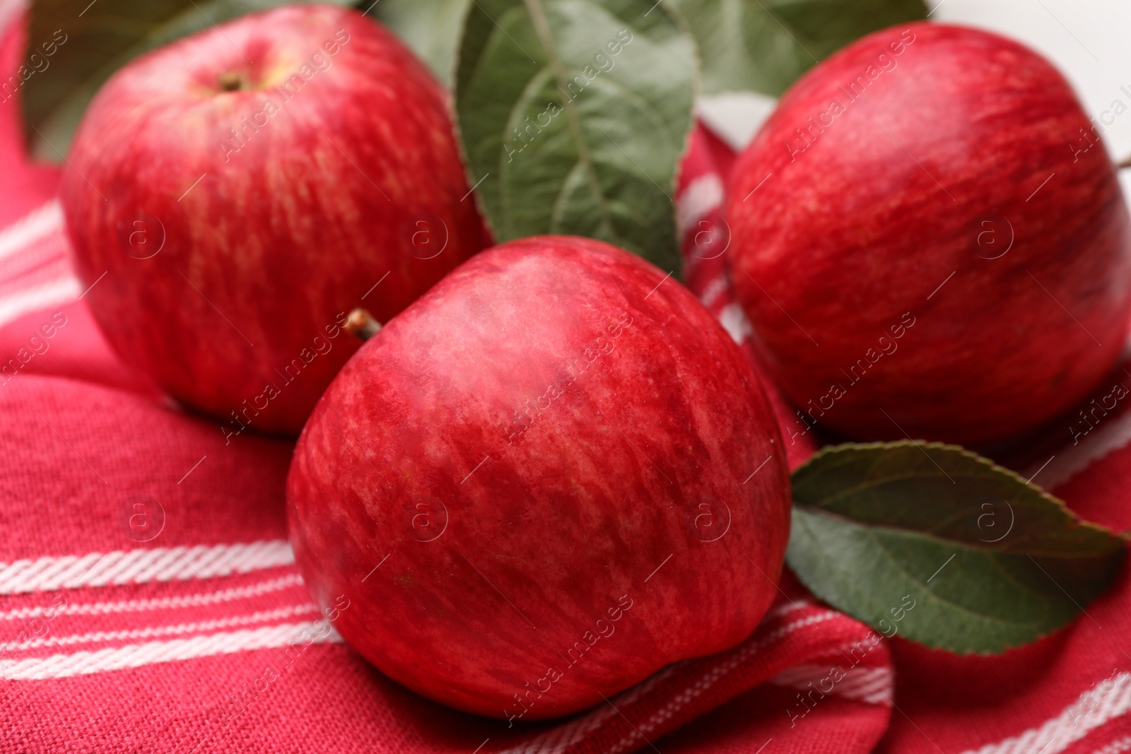 Photo of Fresh red apples with leaves on red cloth, closeup