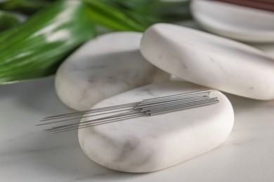 Photo of Acupuncture needles and spa stones on white table, closeup