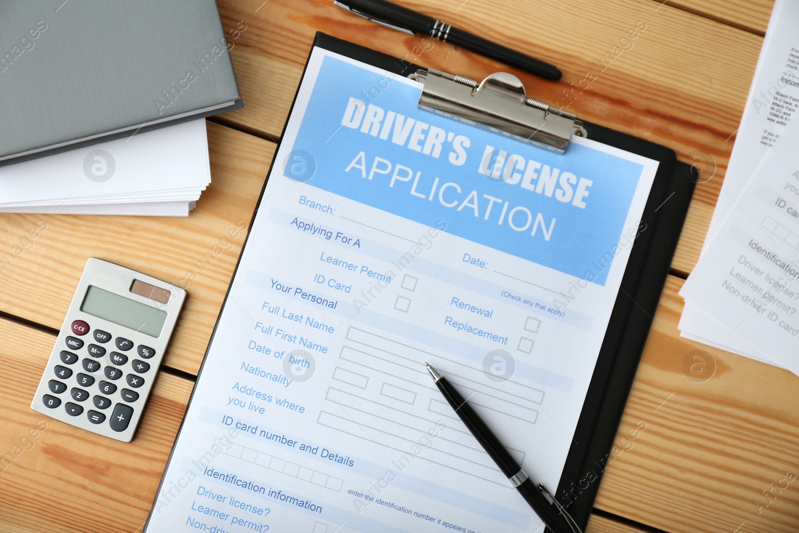 Photo of Driver's license application form, calculator and stationery on wooden table, flat lay