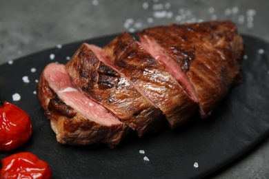Photo of Grilled meat with garnish on slate board, closeup