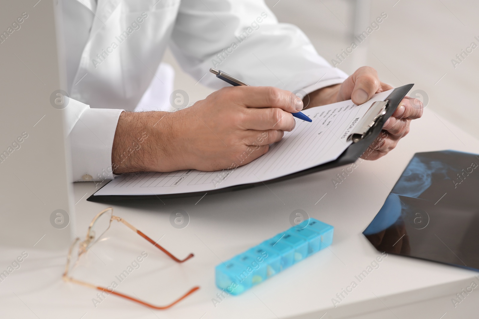 Photo of Doctor filling patient's medical card at table in clinic, closeup